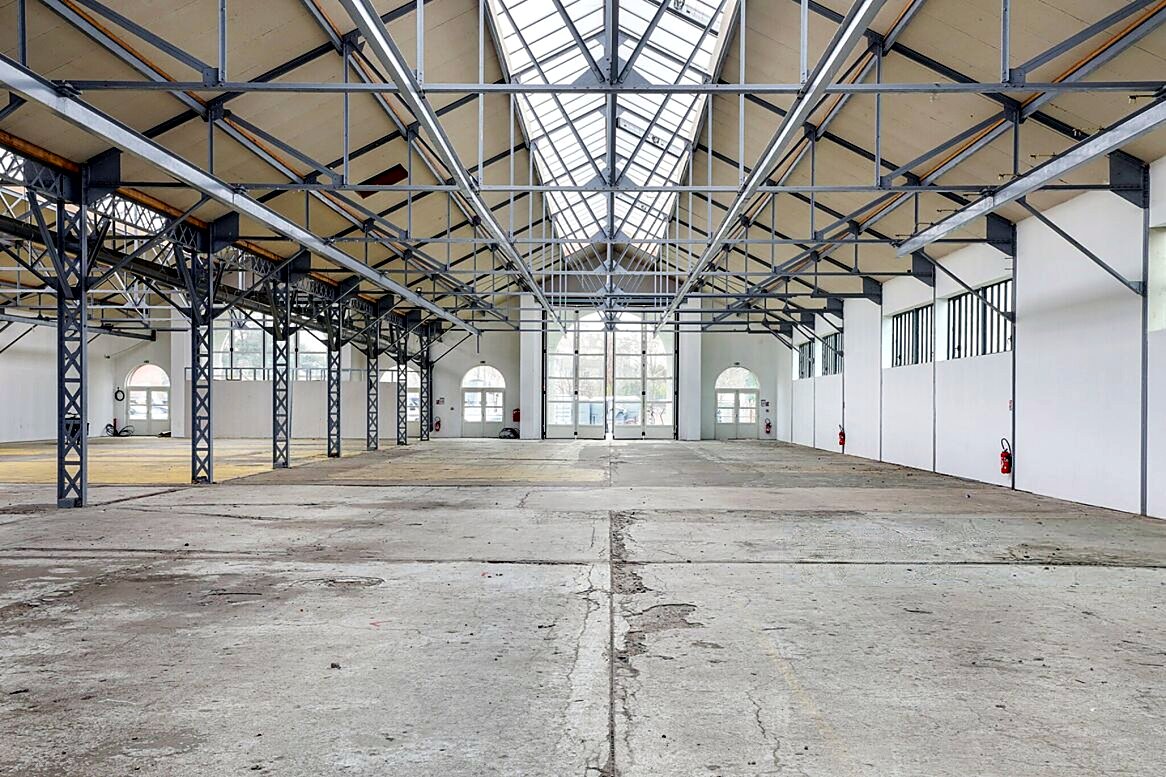 La Grande Halle d'EURĒKA 34 : halle industrielle à charpente métallique et verrière zénithale, portes en arche, sol béton